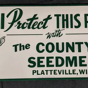 DATED 1979 EMBOSSED TIN SIGN "I PROTECT THIS PLACE" THE COUNTY SEEDMEN PLATTEVILLE WISCONSIN