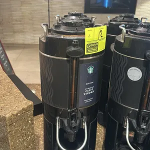 Bunn hot beverage dispenser. Features a black exterior, top carrying handles, front spigot, sight glass, and a drip tray base.