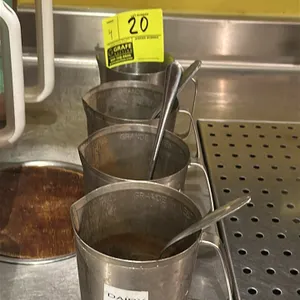 Stainless steel coffee measuring cup. Features a pour spout, side handle, and internal measurement markings.