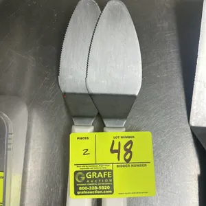 Metal pie knife and spatula. Features a serrated edge and a white handle.