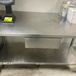 Stainless steel work table. Features a lower shelf and a single drawer. 4'L x 2.5'W. Contents not included.