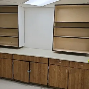 Laminate base cabinet with upper cabinetry. 10'L base cabinet features a wood-grain finish, off-white laminate countertop, drawers, and lower storage.