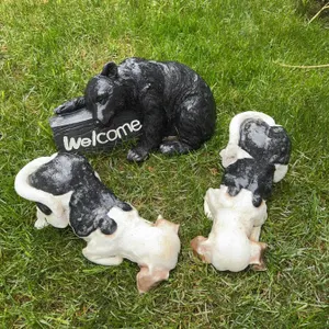 Three animal garden statues: one black bear holding a 'Welcome' sign and two black and white dog fig