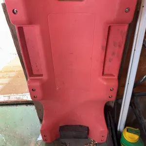 Red plastic rolling creeper with casters, designed for automotive work. Features include built-in ha