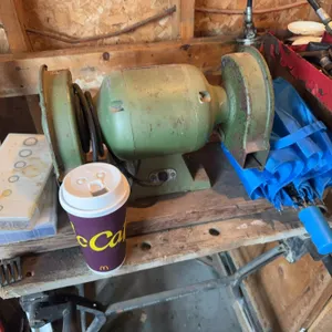 Double wheel bench grinder with a green metal body, mounted on a wooden workbench. This tool is used