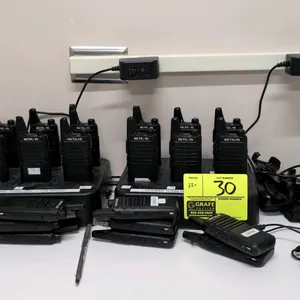 Retevis walkie-talkie. Features a black housing, integrated antenna, and side push-to-talk button. Lot includes (2) 6-slot charging stations, poly hol