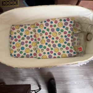 White wicker baby bassinet with folding legs, lace trim, fitted colorful smiley face fabric, and thr