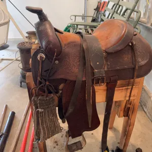 Tooled leather Western horse saddle featuring floral designs, metal conchos, and attached stirrups. 