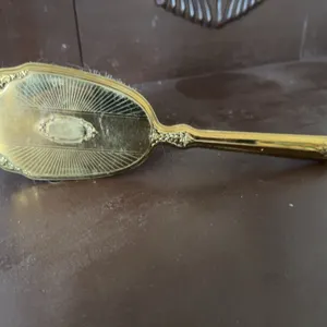 Gold-tone decorative hairbrush featuring ornate detailing on the back and handle and synthetic brist