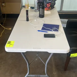 Lifetime poly folding table. Features a white fold-in-half top, gray metal folding legs, and an integrated carrying handle. 5'L. Contents not included