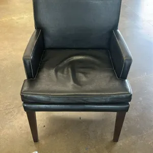 Cushioned armchair featuring black upholstery with white contrast stitching. Supported by four dark wood legs. Note: Seat cushion upholstery is heavil
