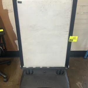 Poly sidewalk sign holder. Features a black plastic frame, white sign board, and wind-resistant springs. Mounted on a fillable polyethylene base desig