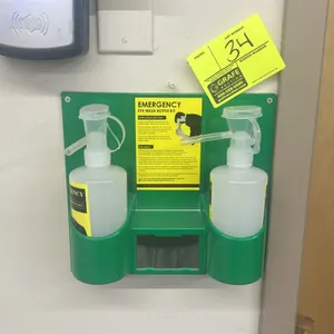 Emergency eye wash bottle kit. Includes (2) squeeze wash bottles and a green plastic wall-mountable bracket. Features an integrated center mirror and 
