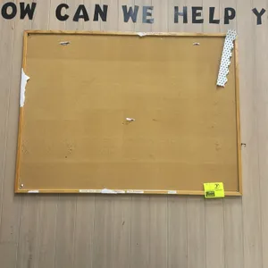 Cork bulletin board. Features a wood frame. 4'x3'. Wall-mounted design. Note: includes paper remnants on the cork surface.