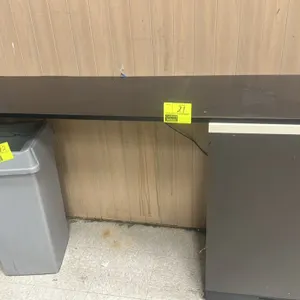 Laminate countertop. Features a black laminate surface supported by one dark gray under-counter cabinet. 6'L. Trash can, side shelving, and surroundin