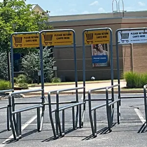 Metal cart corral. Features a double-lane design with tubular metal construction, ground-contact base rails, and integrated 'Please Return Carts Here'