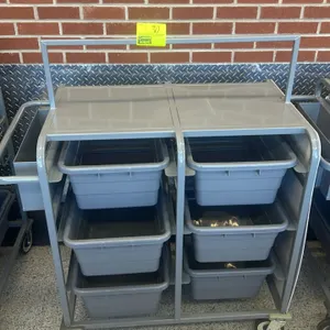 Metal mobile tub rack cart. Features a flat top work surface, a side-mounted hanging utility bin, and slots containing 6 gray poly bus tubs. 26" x 44"