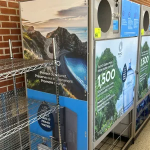 Primo Water self-service bottle exchange and refill station. Features a circular bottle return chute, integrated ticket dispenser slot, graphic side a