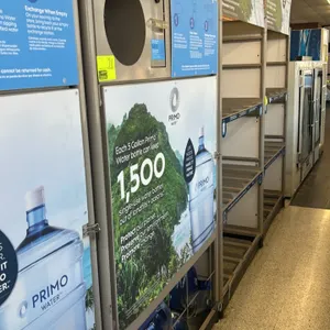 Primo Water self-service refill and exchange station. Features a bottle return drop with ticket dispenser slot, instructional signage, and integrated 