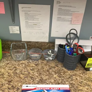 Assorted office desk organizers and supplies. Includes a green perforated plastic basket, a square glass jar, two wire mesh cups with binder clips and
