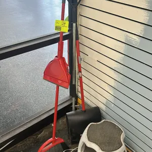Assorted cleaning and facility maintenance supplies. Includes a red upright lobby broom with integrated dustpan, a black upright dustpan with a D-grip