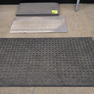 Assorted anti-fatigue mats. Includes one large black rubber perforated mat, one light gray herringbone patterned mat, and two dark gray solid foam mat