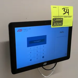 ADP 12" touchscreen tablet time clock. Features a digital keypad display interface for badge entry. Mounted on a black metal wall bracket.