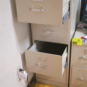 Four-drawer vertical metal filing cabinet in a tan finish. Features metal pull handles and label holders. Includes assorted drawer contents such as of