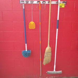 Wall-mounted metal organizer rail with sliding hooks. Includes a corn broom with a wooden handle, a window squeegee and scrubber tool, a cobweb duster