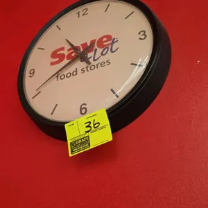 Save-A-Lot branded battery-operated wall clock. Features a black plastic frame and white face with 'Save-A-Lot food stores' logo. 16" Dia.