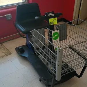 Amigo electric motorized shopping buggy. Features a front wire basket, contoured black plastic seat, finger-pull throttle controls, and an integrated 