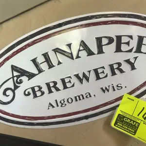An Ahnapee Brewery Metal Sign. (Ahnapee Brewery, 2010s) An oval metal advertising sign for the Algoma, Wisconsin craft brewery. Features stylized blac