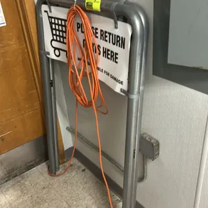 Metal cart return post set. Features tubular metal construction and includes a sign reading "Please Return Carts Here". Note: Extension cord and backg