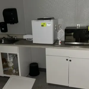 Laminate counter with two white base cabinets, a single-bowl stainless steel sink with faucet, a wall-mounted Triple S plastic soap dispenser, and a w