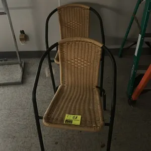 Metal frame armchair. Features a woven tan wicker-style seat and back integrated into a black tubular metal frame with curved armrests. Background ite