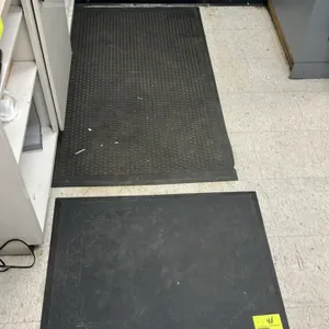 Floor mat lot. Includes one Hubert 36" x 27" black poly floor mat with a patterned border and one 58" x 32" black textured poly floor mat.