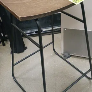Stool featuring a contoured wood saddle seat with a natural grain finish. Mounted on a black metal wireframe sled-style base with an integrated footre