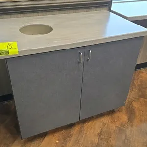 Laminate trash receptacle credenza. Features a solid-surface style top with a trash cutout, two lower doors, a plastic trash bin insert, and two yello