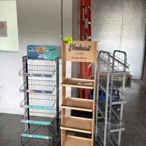 Assorted retail merchandiser display racks. Includes (1) Quaker PopCorners branded black wire 5-tier rack, (1) Elmhurst branded wooden 4-shelf rolling