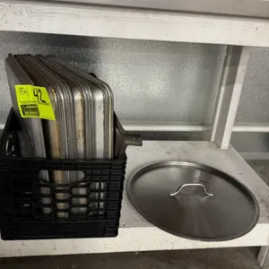 Lot of 15+ metal sheet pans and a lid. Features 12"x18" metal sheet pans. Includes one circular metal lid with a center handle. Plastic crate included