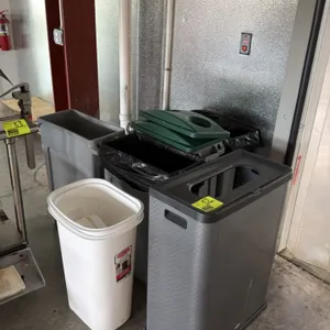Assorted poly trash cans with covers. Includes a white Rubbermaid slim receptacle, a grey slim receptacle, a textured grey decorative receptacle with 