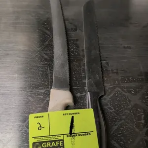 Assorted stainless steel serrated kitchen knives. Includes (1) knife with a textured white plastic handle and (1) knife with an integrated stainless s