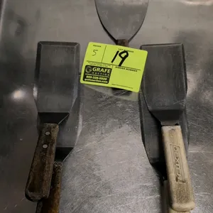 Assorted metal kitchen spatulas. Includes (5) commercial-grade spatulas and scrapers featuring (2) wooden-handled offset turners, (2) white plastic-ha