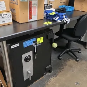 Unbranded wall-mount workstation table. Features a black Formica laminated top, two cylindrical stainless steel front legs, and a rear wooden wall-mou