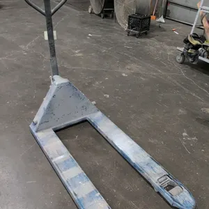 Manual pallet jack featuring blue painted steel construction, a loop handle with integrated control lever, dual steer wheels, and tandem front load ro