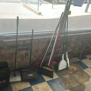 Assorted commercial cleaning supplies. Lot includes multiple upright angled brooms and lobby-style stand-up dustpans. Features synthetic bristle broom