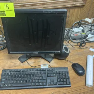 Dell 18" monitor with wired keyboard and wired mouse. Features black finish. Mounted on a desktop stand. Computer tower, speaker, and background desk 
