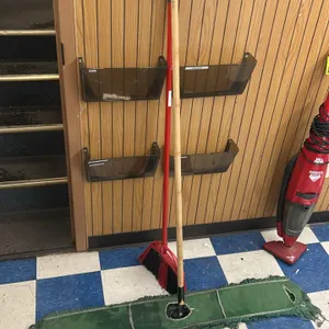 Cleaning supply lot. Includes one green dust mop with a wood handle, one angle broom with red synthetic bristles, and one gray round poly trash can mo