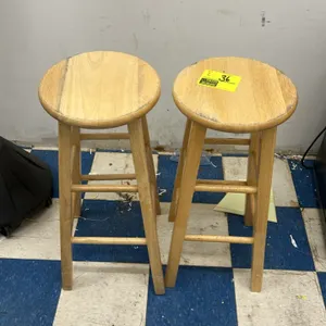 Wooden barstool. Features a round solid wood seat in a natural finish, four tapered legs, and integrated dual-height footrest rungs.