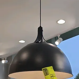 Black dome pendant light. Features a white interior shade, decorative top strap accents, a single-light socket, a black hanging cord, and a matching r